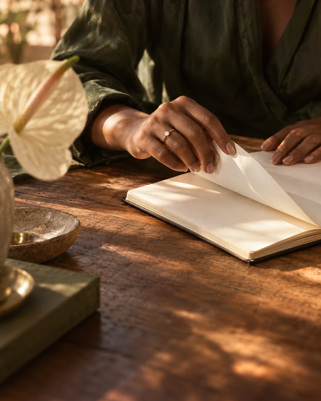 A hand turns a notebook page beside a softly lit cream flower.