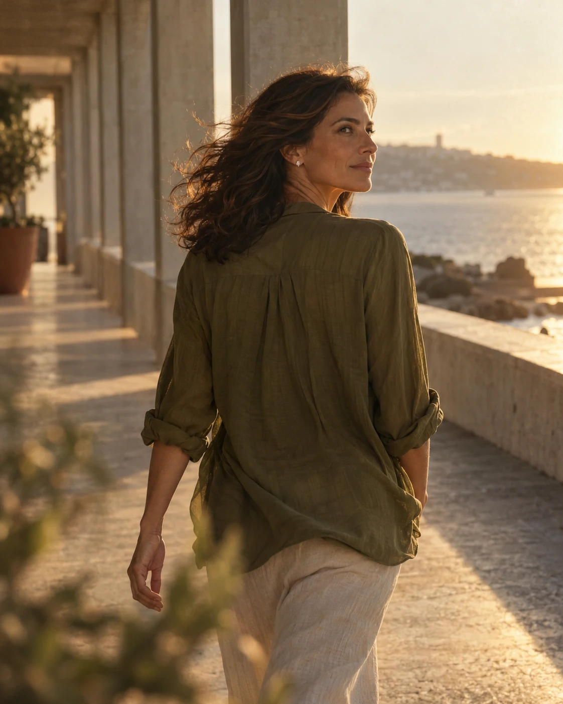 A woman walks through a coastal colonnade in late afternoon light.